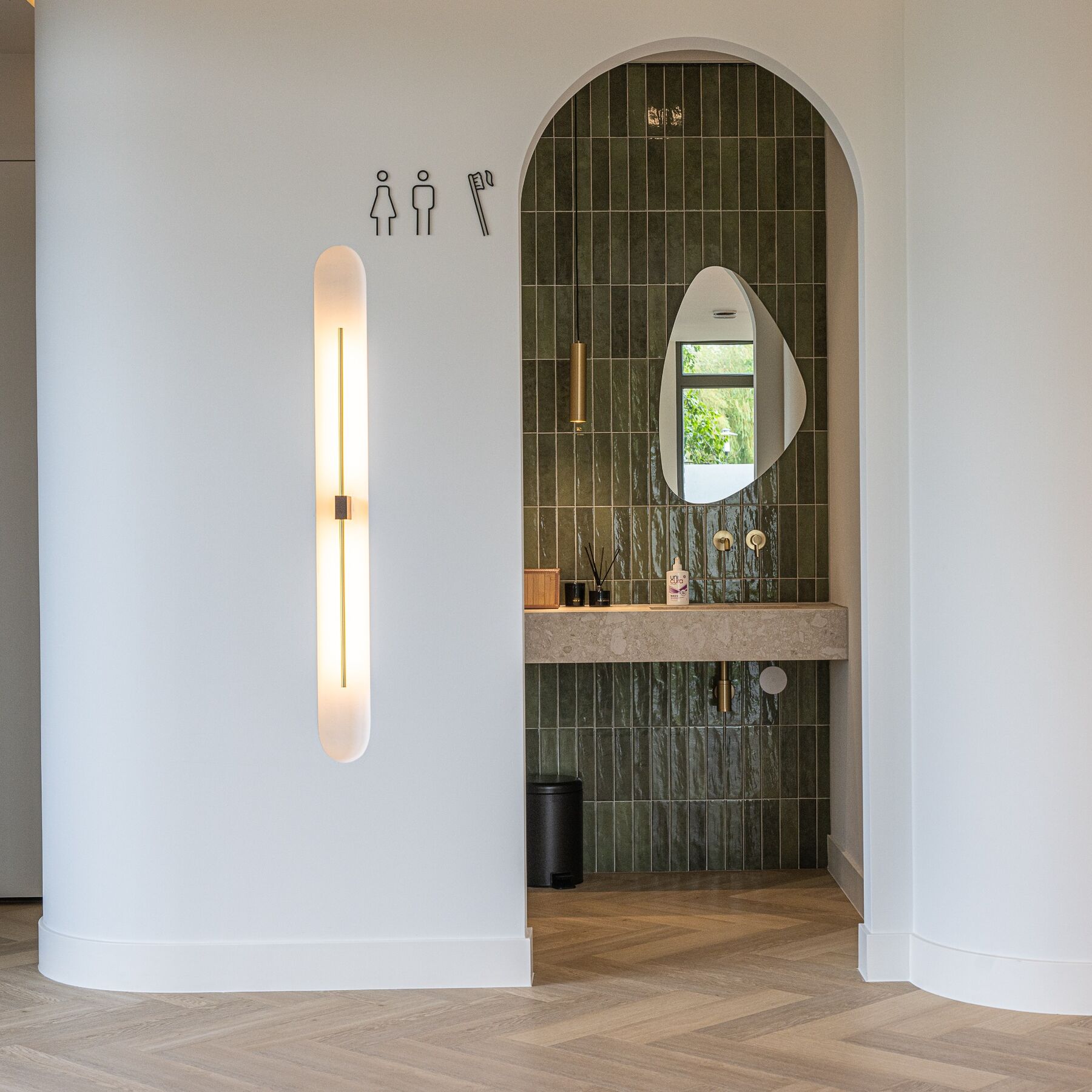 Boogvormige wastafelnis met groene tegels en messing details